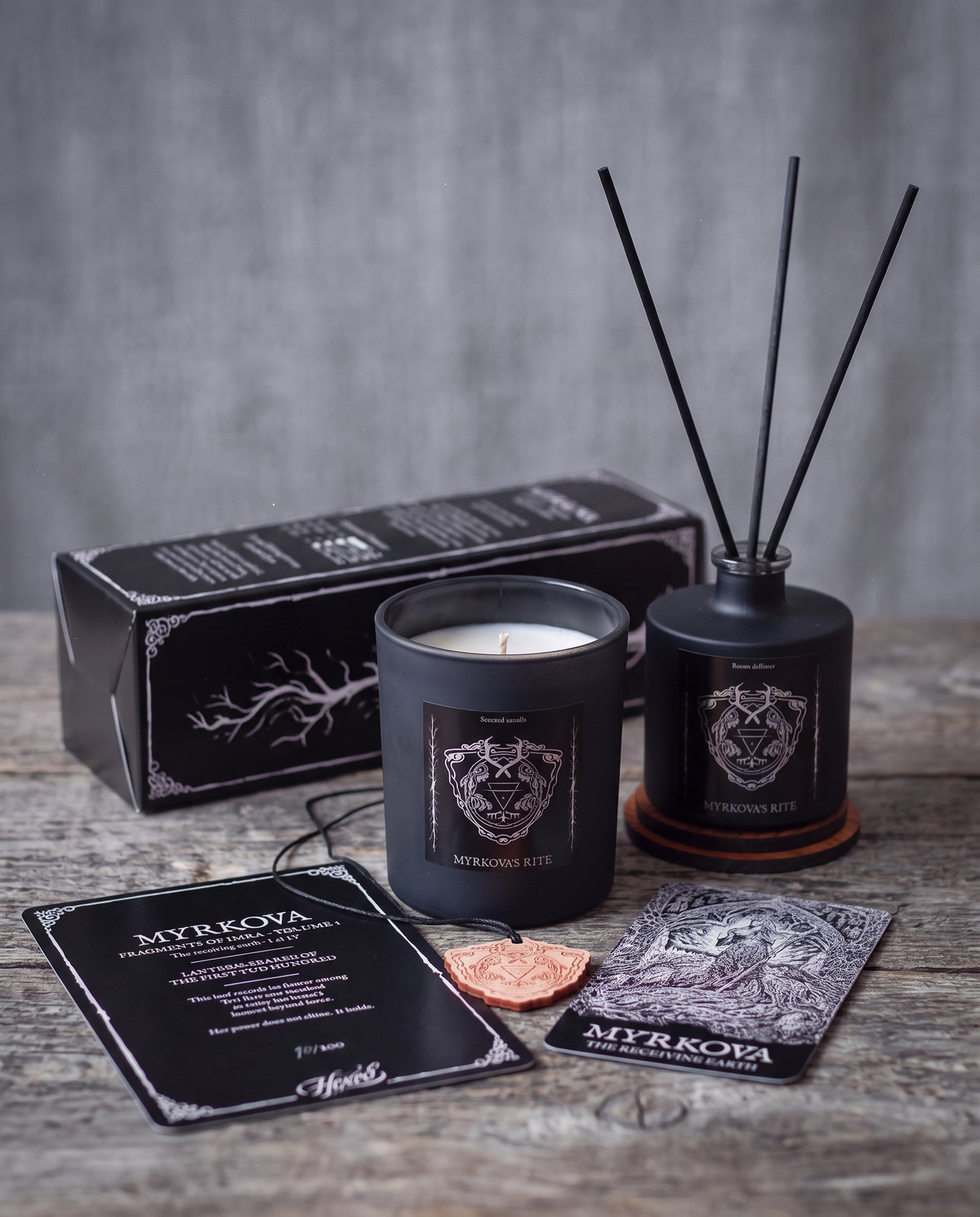 Myrkova's Rite First Edition bundle by HEXED on a weathered wooden surface: scented candle, room diffuser with black reeds, black illustrated gift box, numbered Fragments of Imra lore card, wooden crest pendant and the Myrkova goddess card